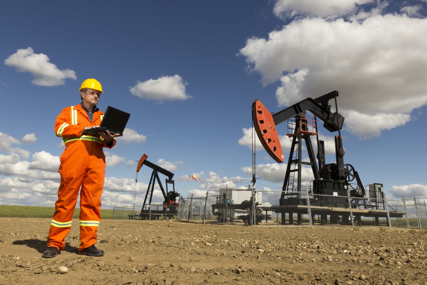 An image from the oil industry of an engineer and computer working at a pair of pumpjacks.