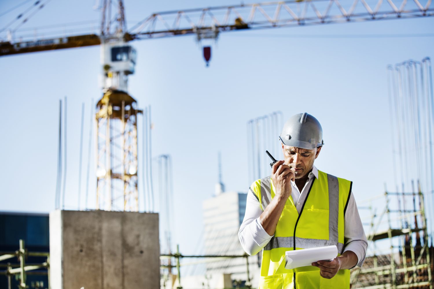 Architect using walkie-talkie while reading document at construction site